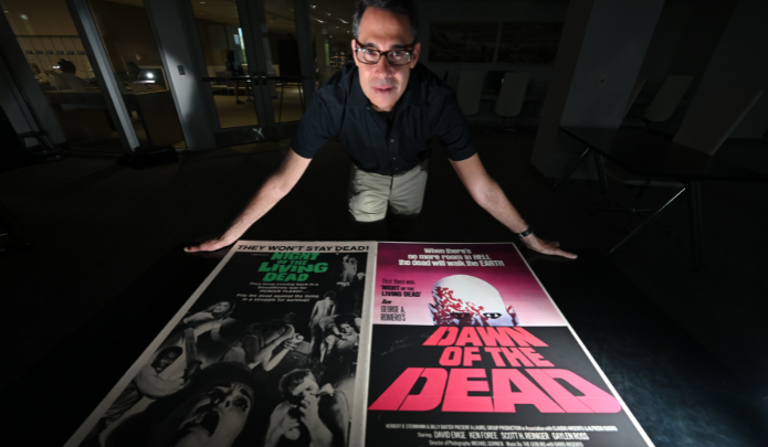 Professor Adam Lowenstein standing over 2 movie posters