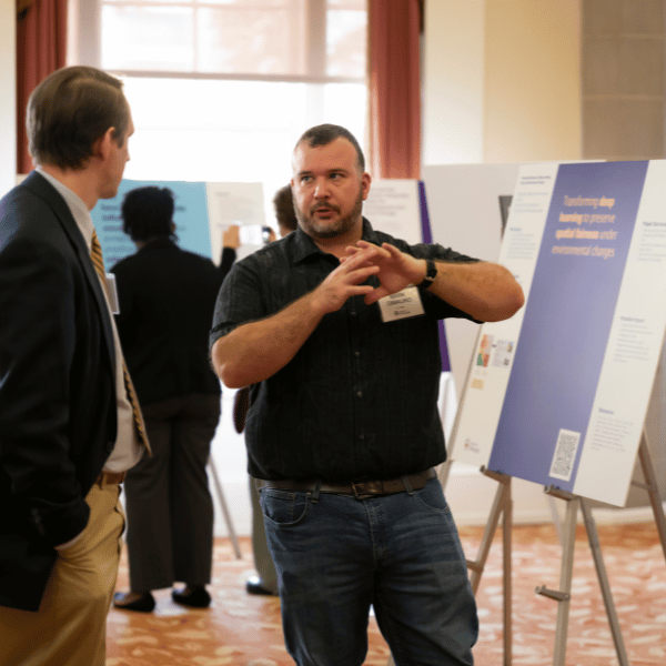two men speaking in front of a research poster
