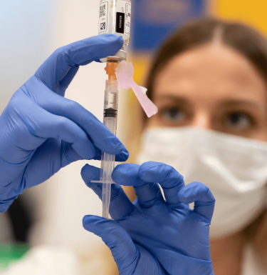 woman in blue gloves holds vial and needle